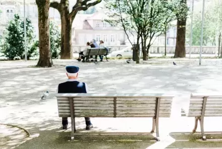 older man sitting on bench staring in park