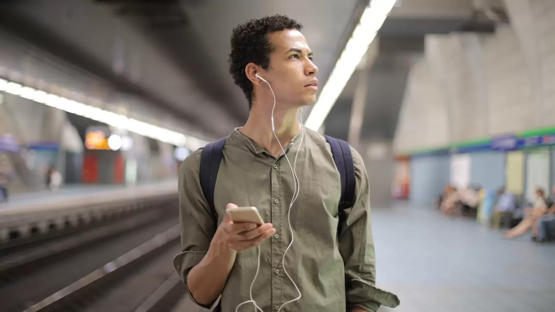 person wearing headphones while holding phone and looking to the side in a subway station