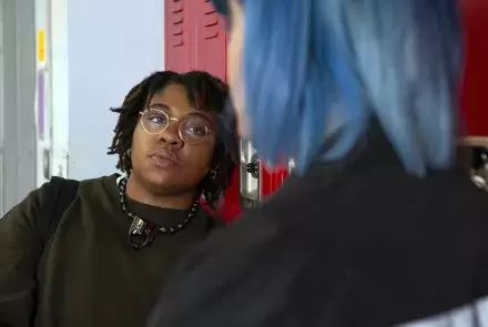 Non-binary student talking to a friend in front of their locker